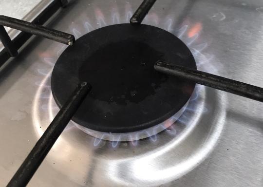 a gas hob burner turned on with a blue flame