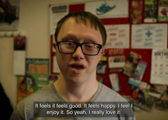 A screenshot of the active together film. A young Disabled man, Thomas is seen wearing a grey t shirt, with short brown hair and black square rimmed glasses. The caption reads 