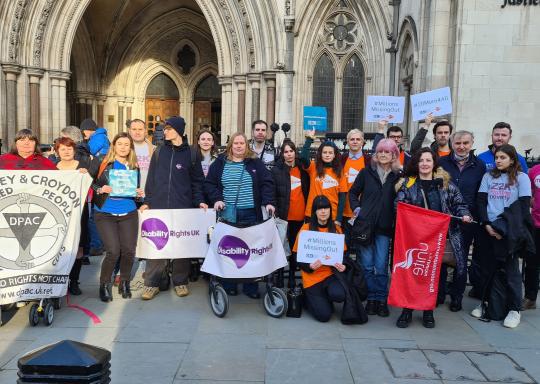A group of campaigners stand outside a court holding banners