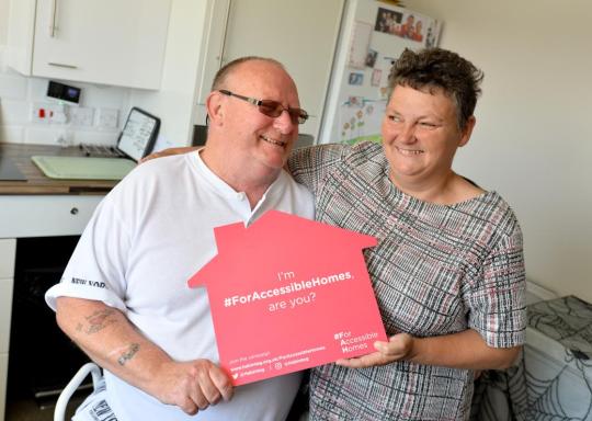 Two people embrace while holding a sign reading 