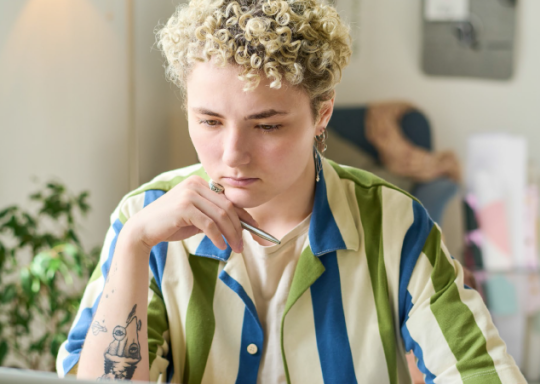 Young person with tattoos and a prosthetic arm working at a laptop computer