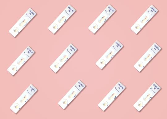 A number of Covid 19 lateral flow tests against a pink background.