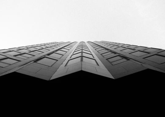 Black and white image of the front facade of a modernist block of flats. The building shape repeats all the way up.