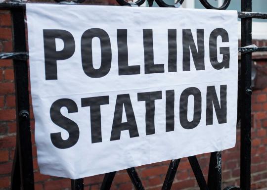 A white banner on a black fence which reads 