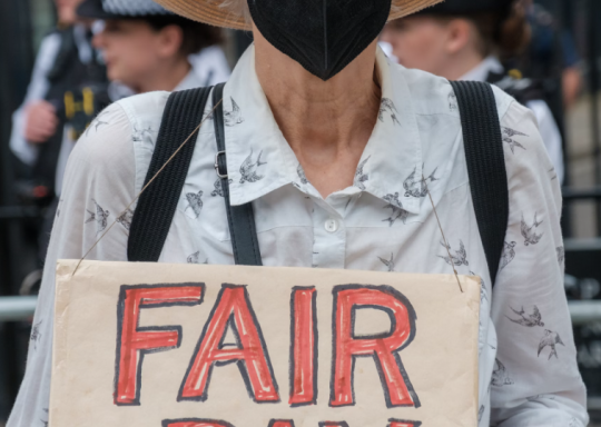 Person in a COVID Mask holding a protest sign that says Fair Pay