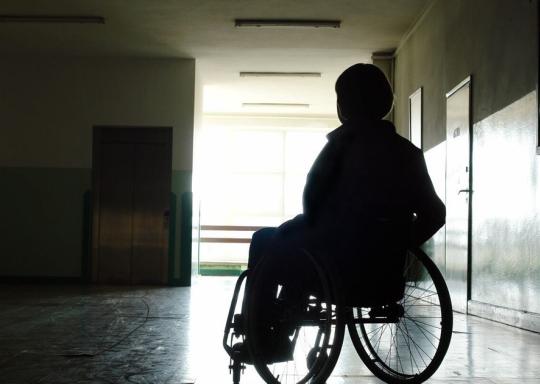 Images shows wheelchair user in a deserted hallway, wheelchair user in shadow.