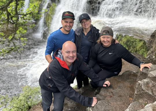 4 smiling trekkers standing on a rock by a waterfall