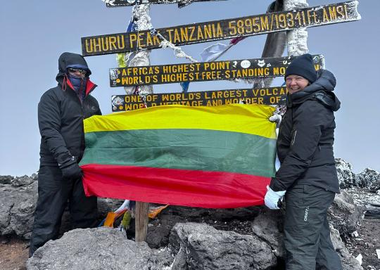 Picture of two trekkers in walking gear at the summit of Kilimanjaro, holding a Lithuanian flag