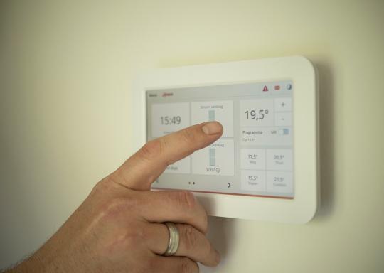 Image shows a hand about to use the touch screen on a wall mounted heating control