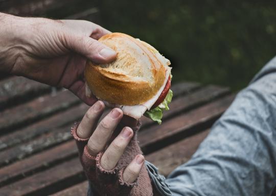 image shows a sandwich being handed to a person wearing fingerless gloves.