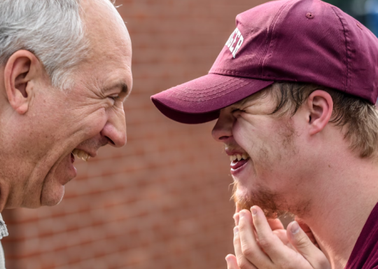 Image of a father and son laughing at each other. The son has Down's syndrome