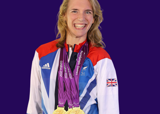 Image of Sophie Christiansen with multiple gold medals around her neck, smiling in an London 2012 Olympic outfit