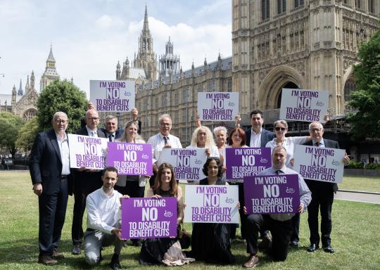 Image of 15 MPs outside Parliament holding DPO Forum 'Vote NO to benefit cuts' placards