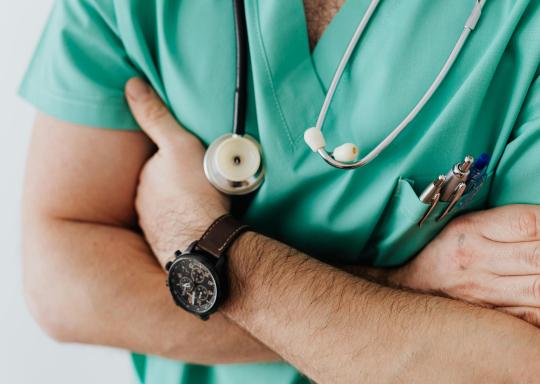 Doctor in scrubs with hands folded wearing a stethoscope 