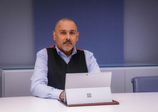 Kamran Mallick, Disability Rights UK sits in front of a laptop