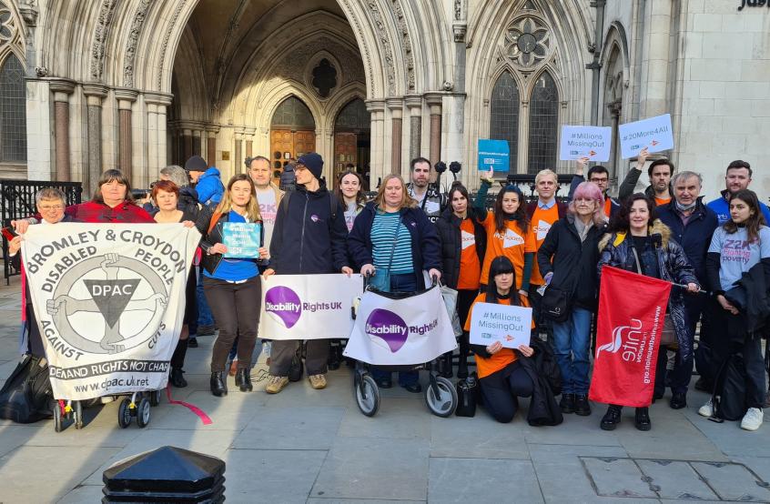 A group of campaigners stand outside a court holding banners