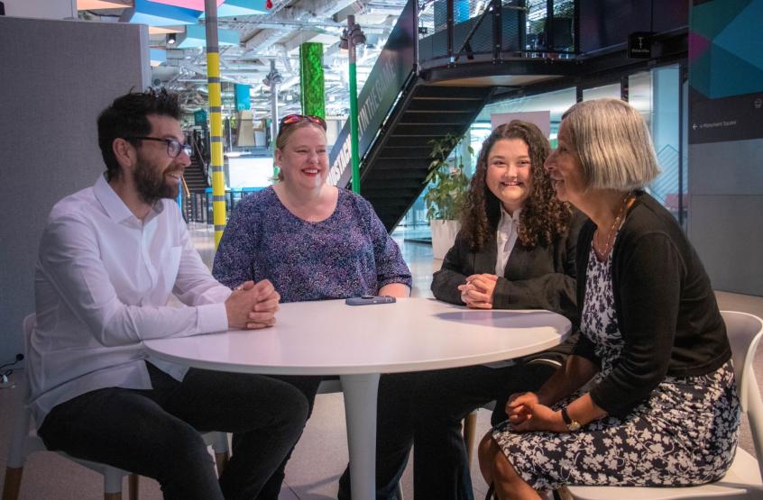 Four people sat around a table smiling at each other, one male three female