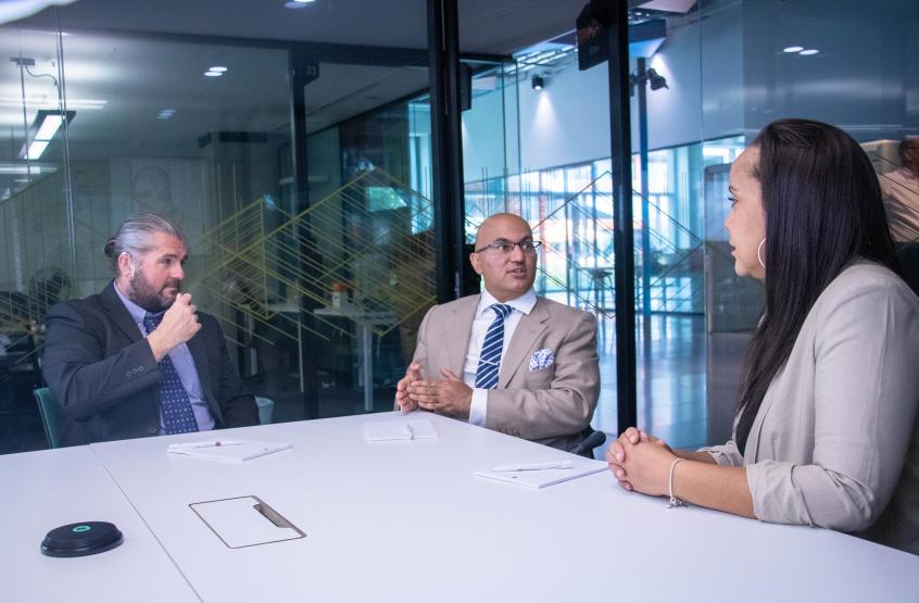 Three people sat around a table inside a glass meeting room in discussion