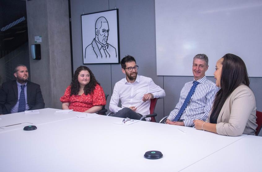 A group of five people sit around a table smiling and talking